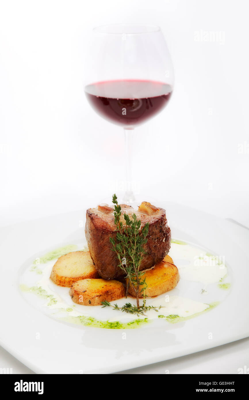 Carne arrosto con patate su piastra bianca con bicchiere di vino Foto Stock