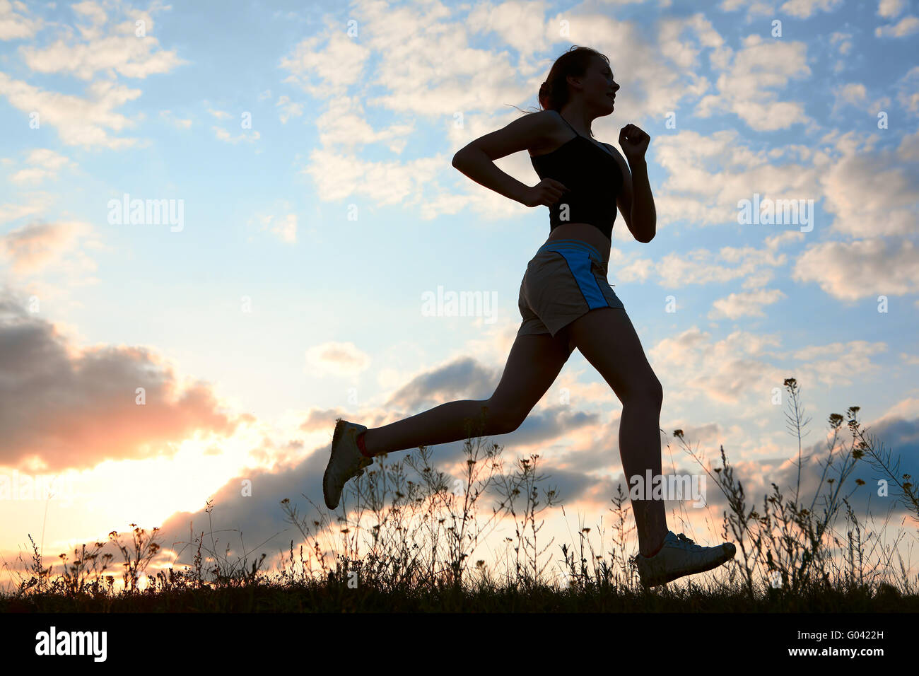 Silhouette donna correre sotto il cielo blu con nuvole Foto Stock