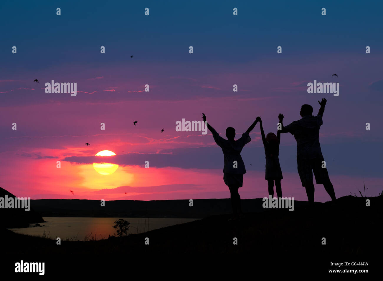 La famiglia da tre persone accoglie il sole al tramonto Foto Stock