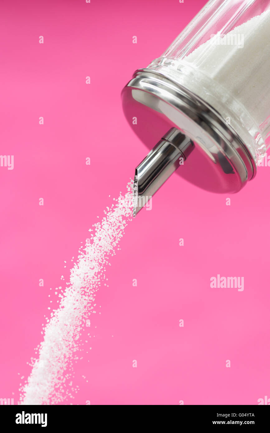 Dosatore zucchero versando contro sfondo rosa Foto Stock