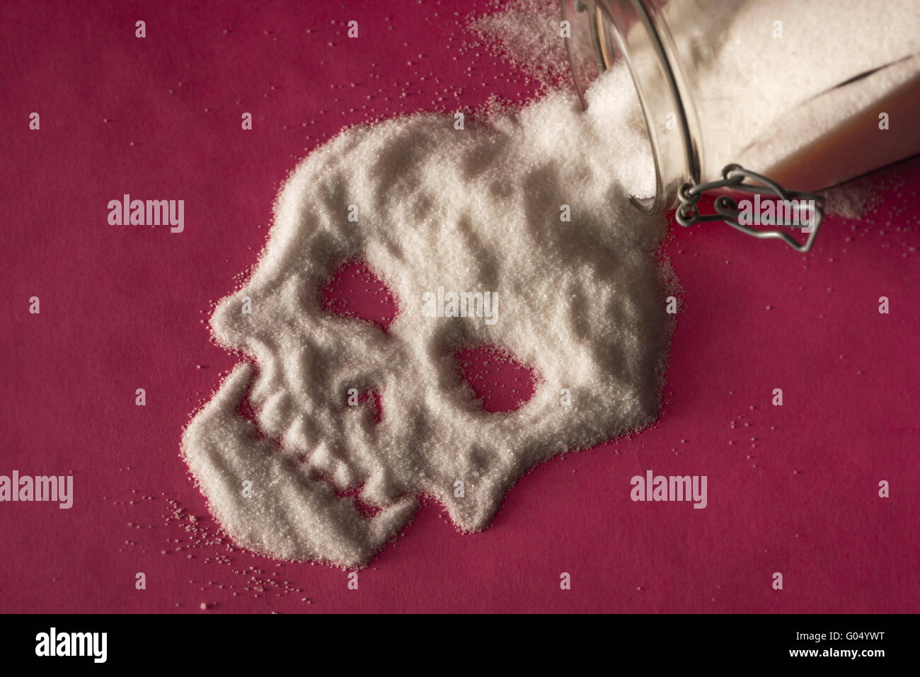 Lo zucchero bianco di fuoriuscita del vasetto di vetro su sfondo rosa e formando una faccia del cranio Foto Stock
