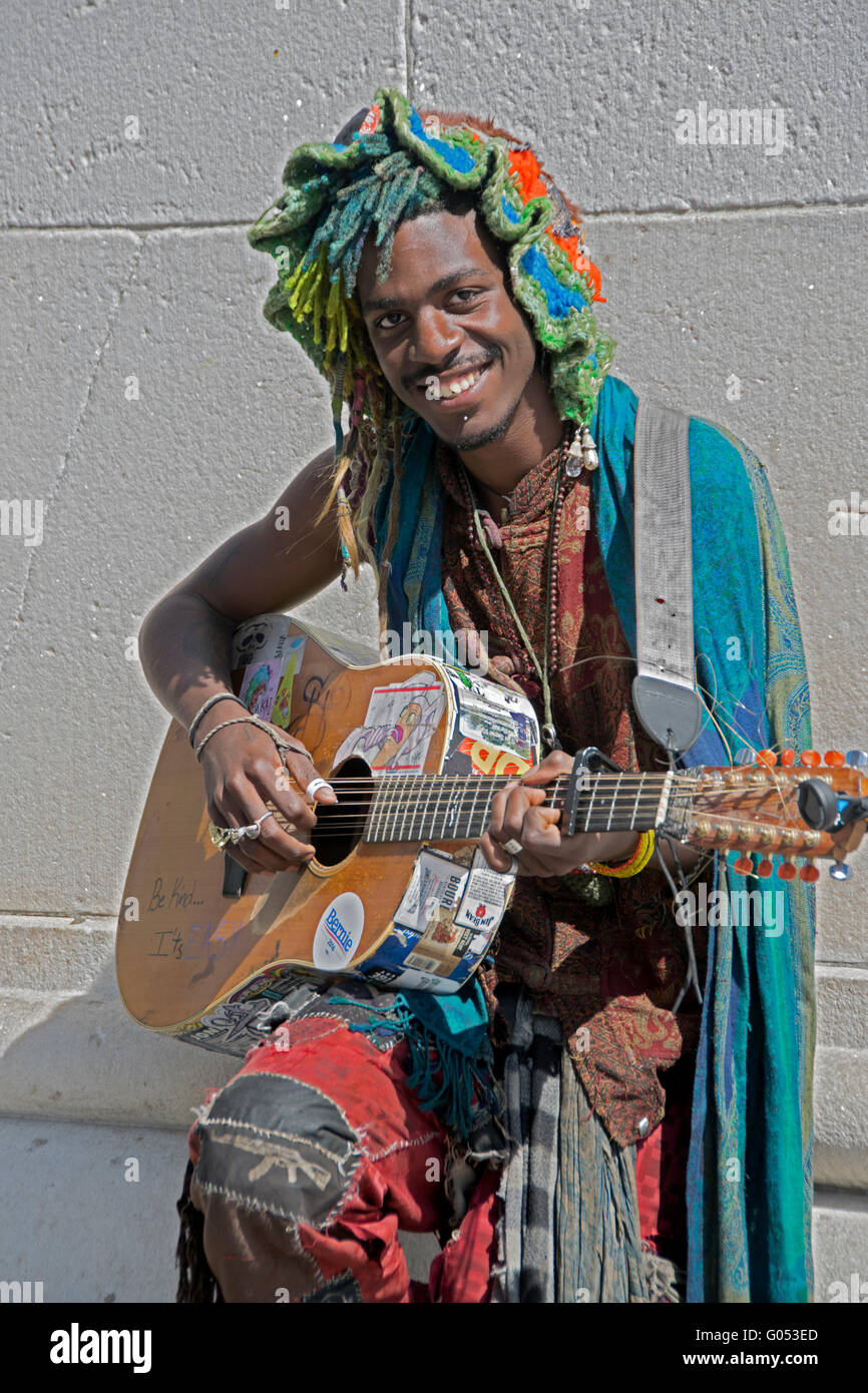 Ritratto di un suonatore ambulante in un colorato hat & outfit suonare e cantare con la chitarra in Washington Square Park di New York City Foto Stock