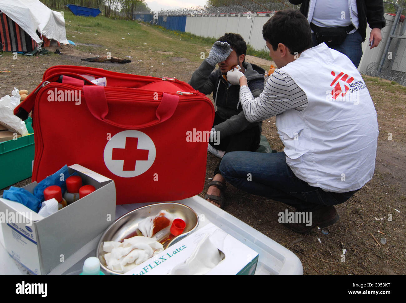 Il Dottor Vladimir Andric, MSF il Capo della Clinica Mobile, considera un rifugiato ferito in faccia. In retro-massa la parete e barbe Foto Stock