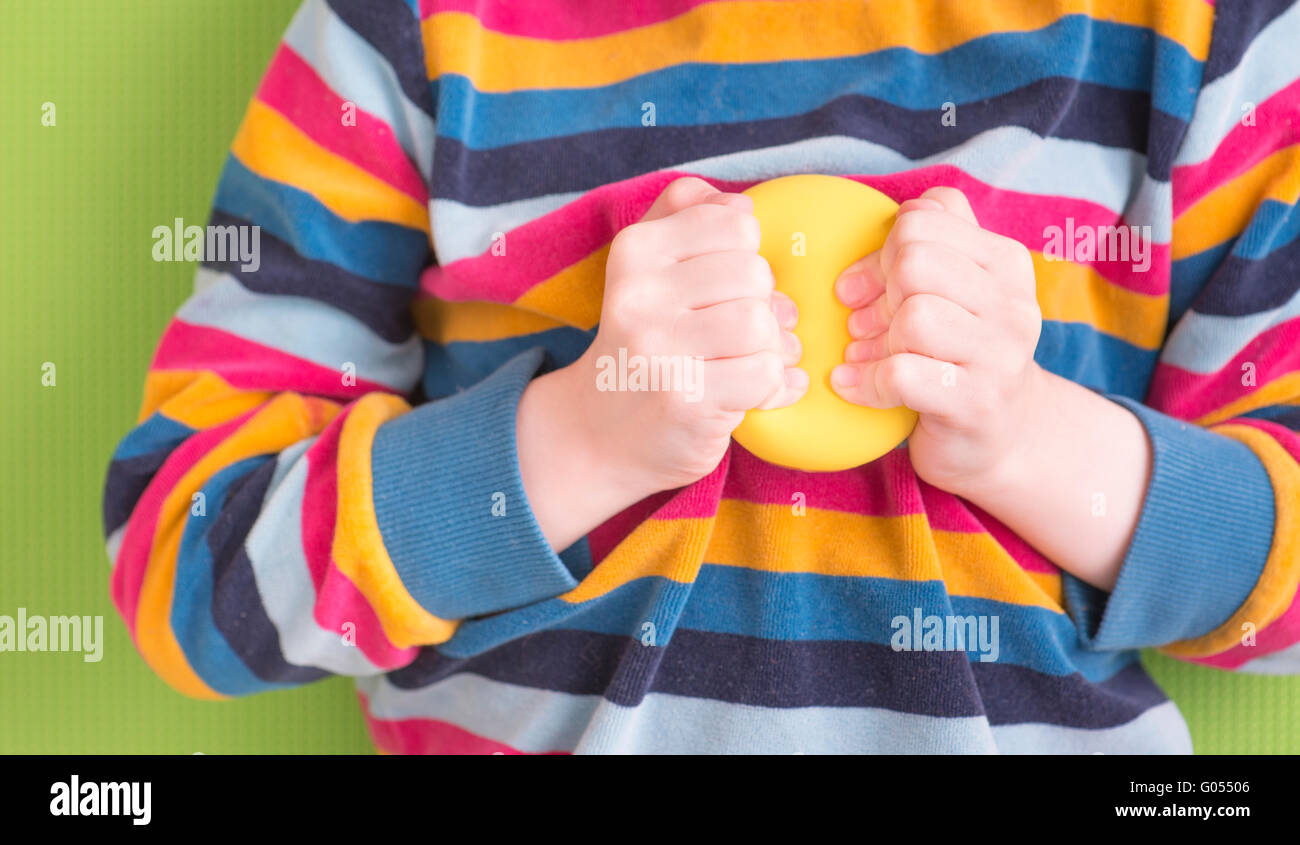 Bambino holding e la strizzatura giallo palla con le mani. Concetto di infanzia ansia e frustrazione e rabbia. Anche un simbolo di Foto Stock