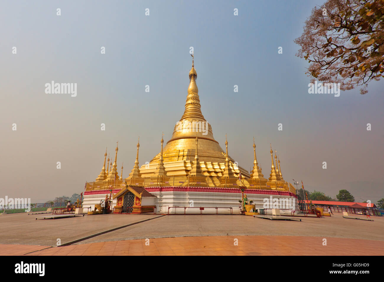 Oro gigante stupa di Tachileik Shwe Dagon Pagoda in Myanmar luccicante nella luce del sole con le persone camminare e pregare nei santuari Foto Stock