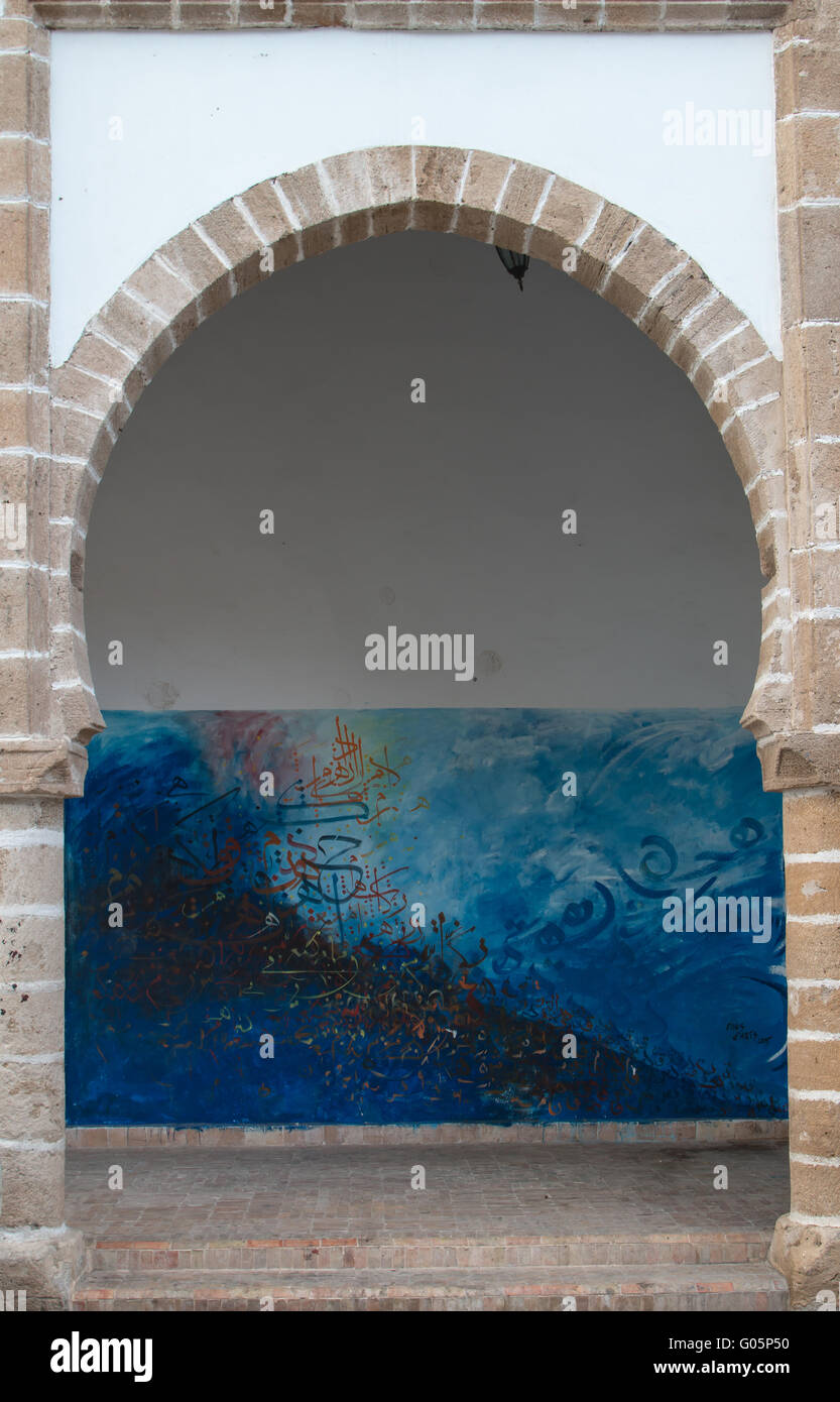 Edificio con facciata bianca e un arco tradizionale. Coloratissimo graffito in background. Essaouira, Marocco. Foto Stock