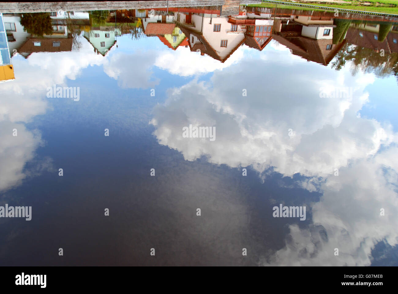 La riflessione di case e di cielo nel laghetto del paese Foto Stock