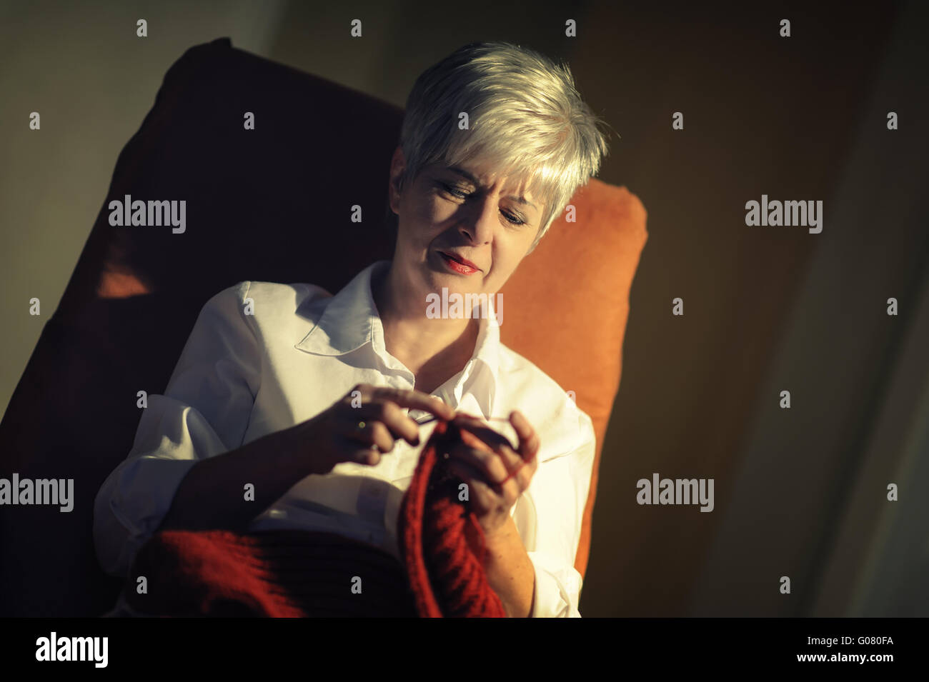 Una donna anziana seduti in poltrona e maglieria a s Foto Stock