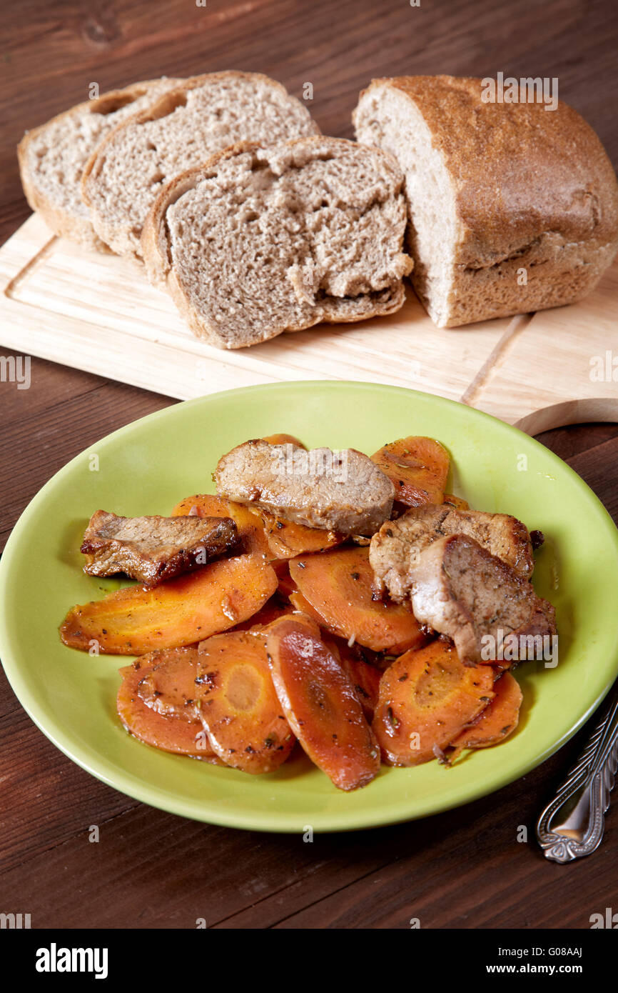 Il piatto con la carne e le carote tagliate il pane su un tavolo da cucina Foto Stock