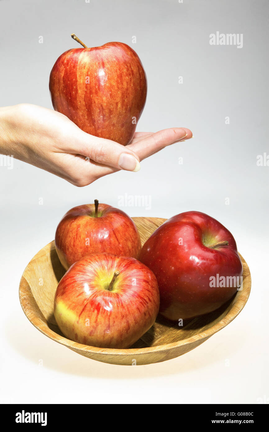 La mano trattiene un Apple e una ciotola con le mele rosse Foto Stock