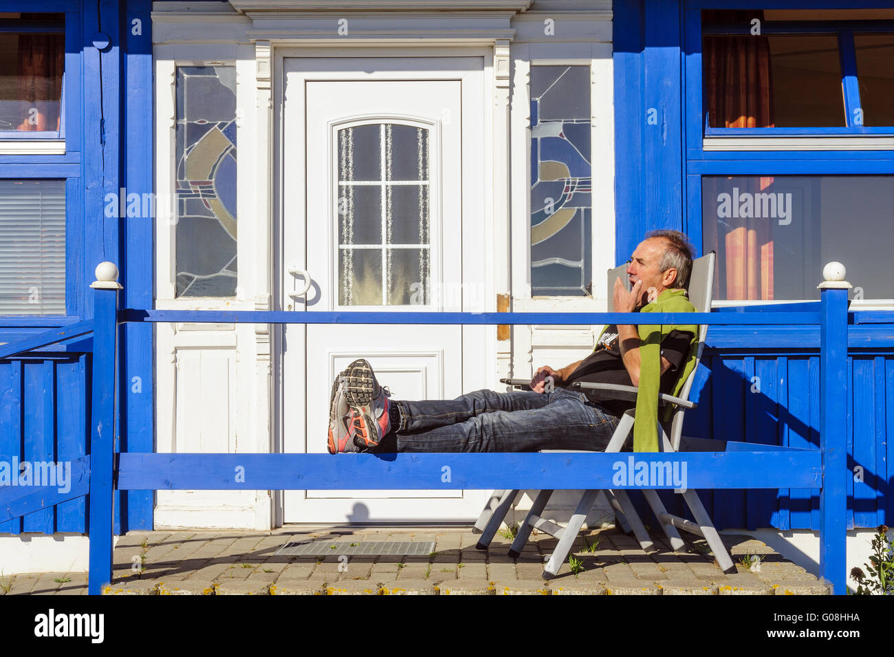 Uomo seduto rilassato sulla veranda della sua casa Foto Stock