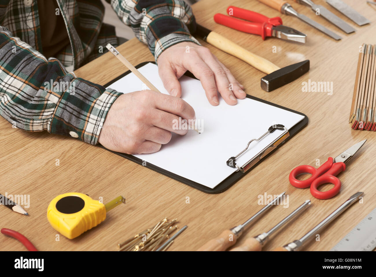 L'uomo delineando un progetto DIY su un blocco appunti con gli strumenti di lavoro tutto intorno, le mani vicino, hobby e concetto di artigianato Foto Stock