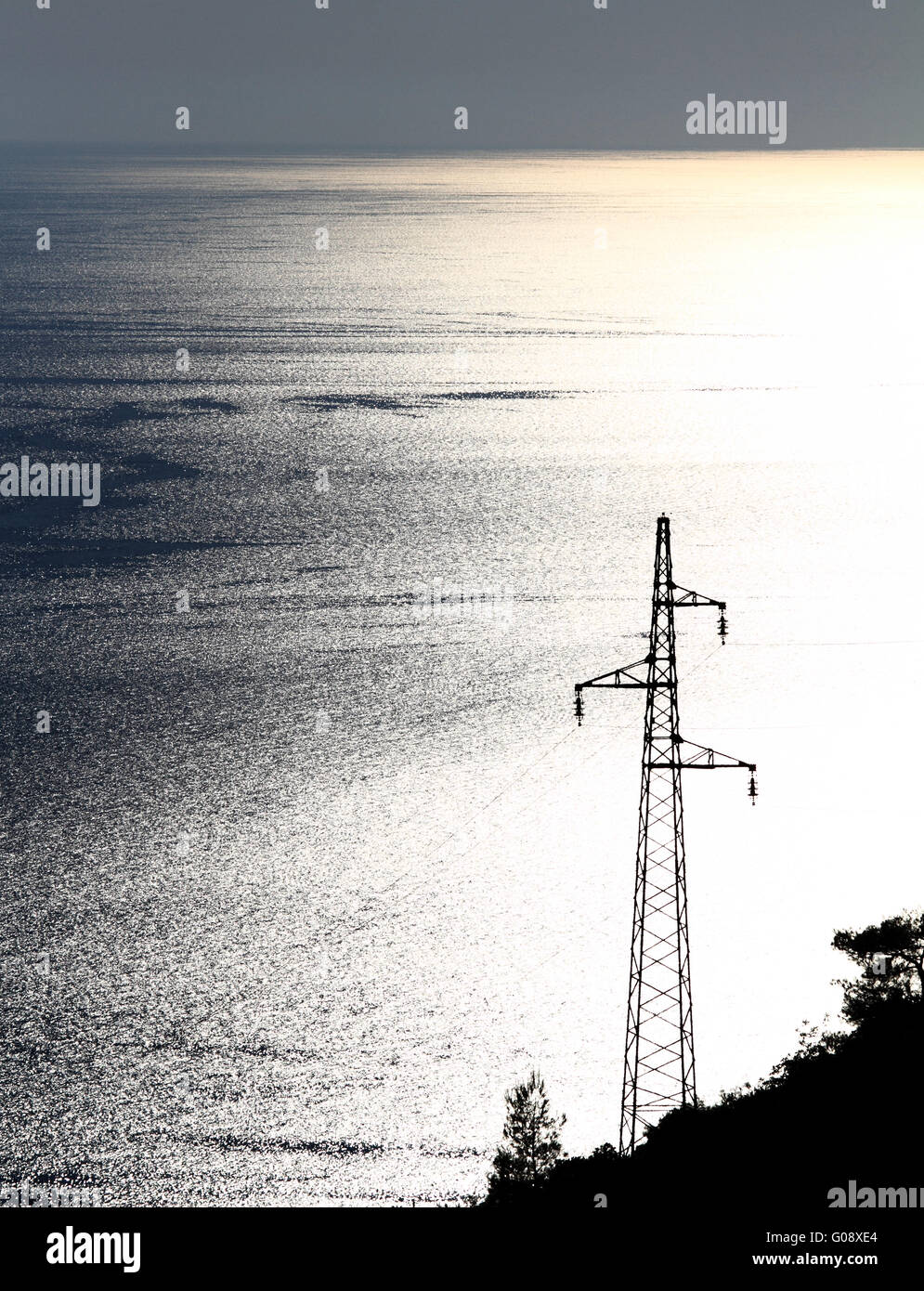 Elettricità pilone con molti cavi sul blu e giallo mare Foto Stock