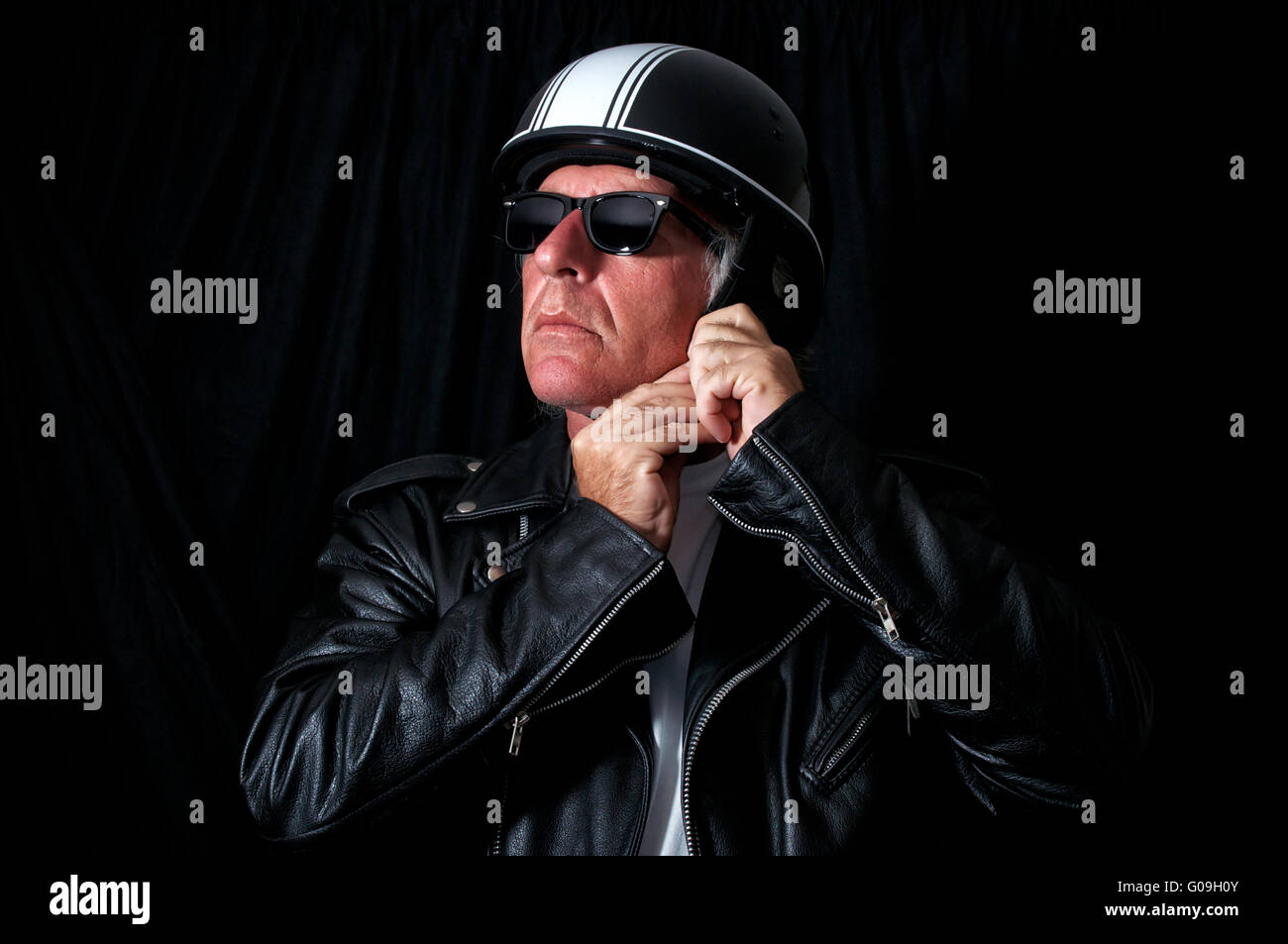 Studio shot del biker maschio / motociclista indossare nero vintage giacca  di pelle e occhiali da sole mettendo sul casco retrò. Preparazione per moto  Foto stock - Alamy