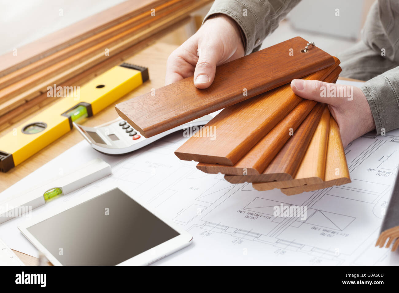 Professional interior designer azienda campioni di legno per la zoccolatura e battiscopa, mani close up con desktop, casa blueprint, t Foto Stock