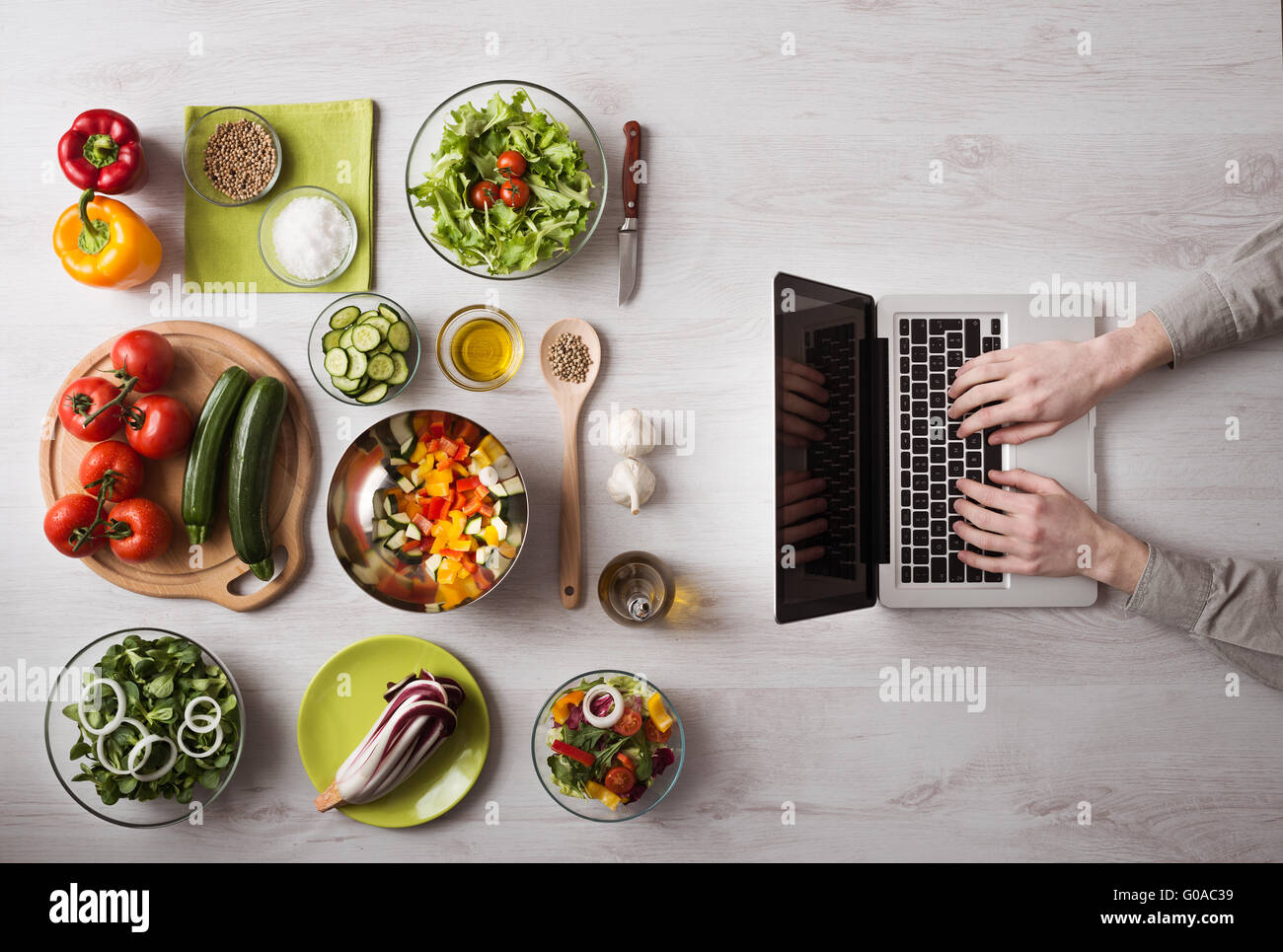 Uomo in cucina la ricerca di ricette sul suo computer portatile con ingredienti alimentari e di verdure fresche a sinistra, vista dall'alto Foto Stock