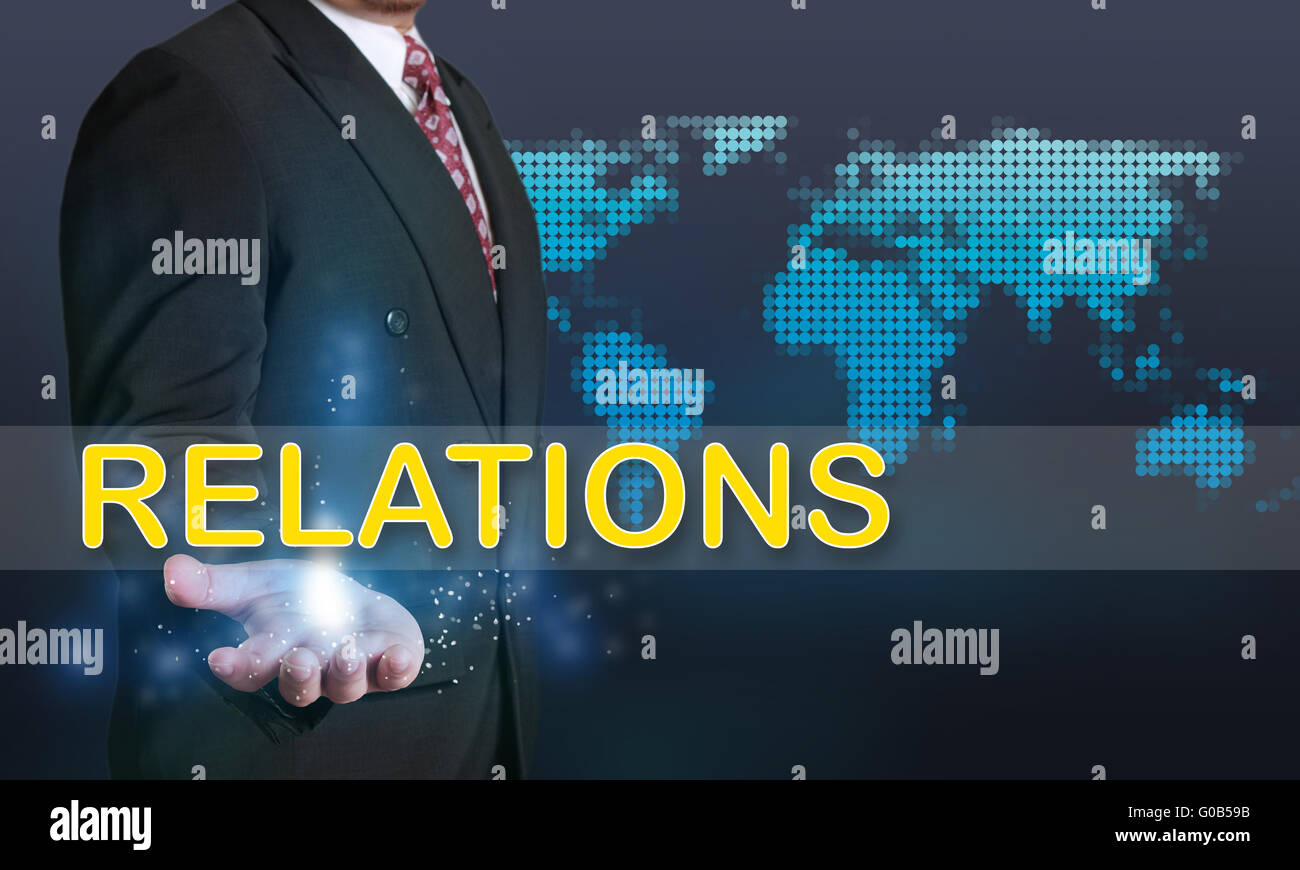 Il concetto di Business immagine di un imprenditore che mostra le relazioni parola sulla sua mano su sfondo blu con tratteggiata la mappa mondiale Foto Stock