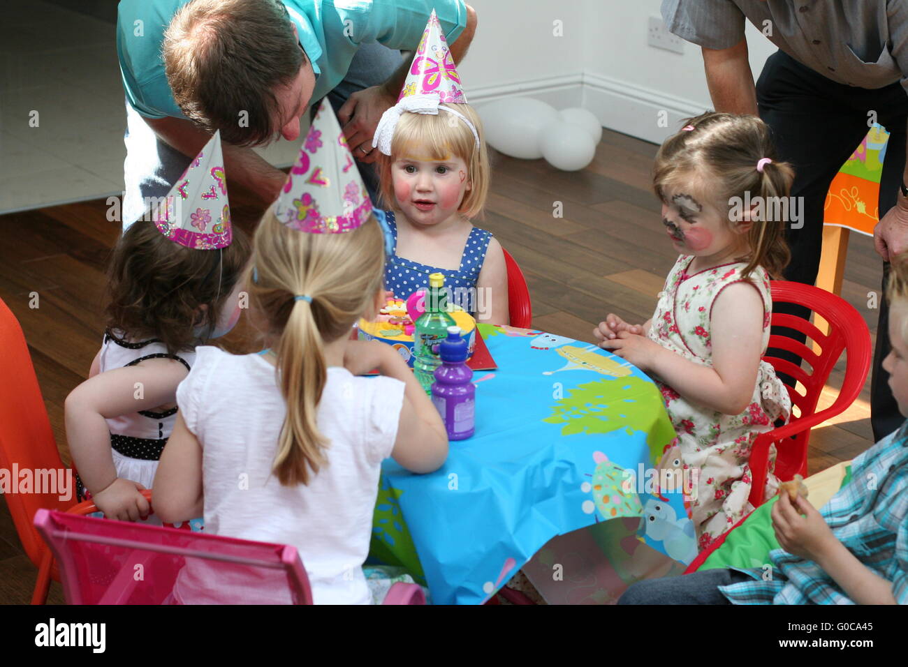 Bambini /ragazzi festa di compleanno, bambini seduti attorno al tavolo di  partito due anni di indossare la faccia parte di vernice cappelli pigtail,  e per il divertimento di tutta la famiglia, il