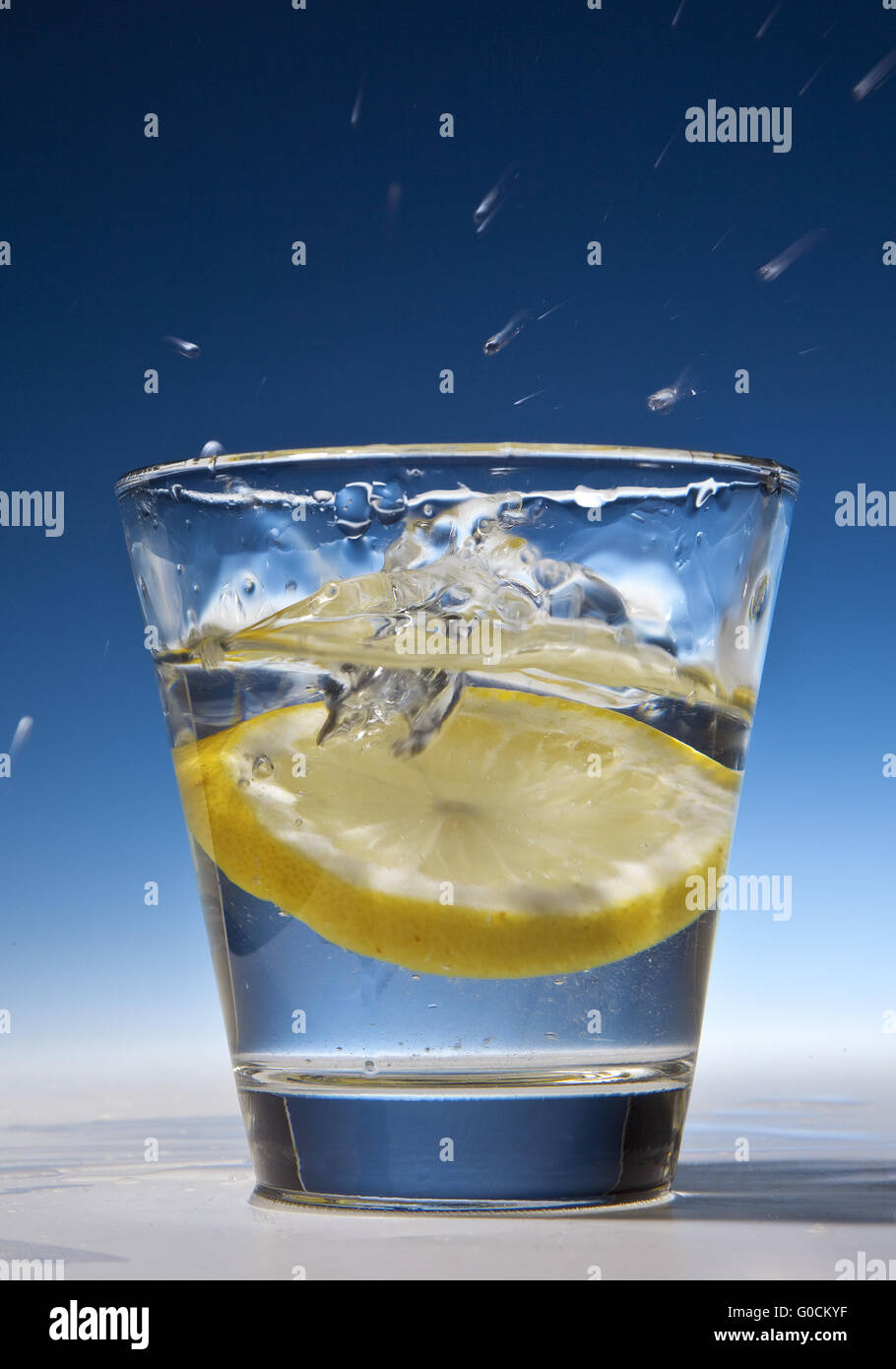 Fettina di limone di cadere in un bicchiere con acqua Foto Stock