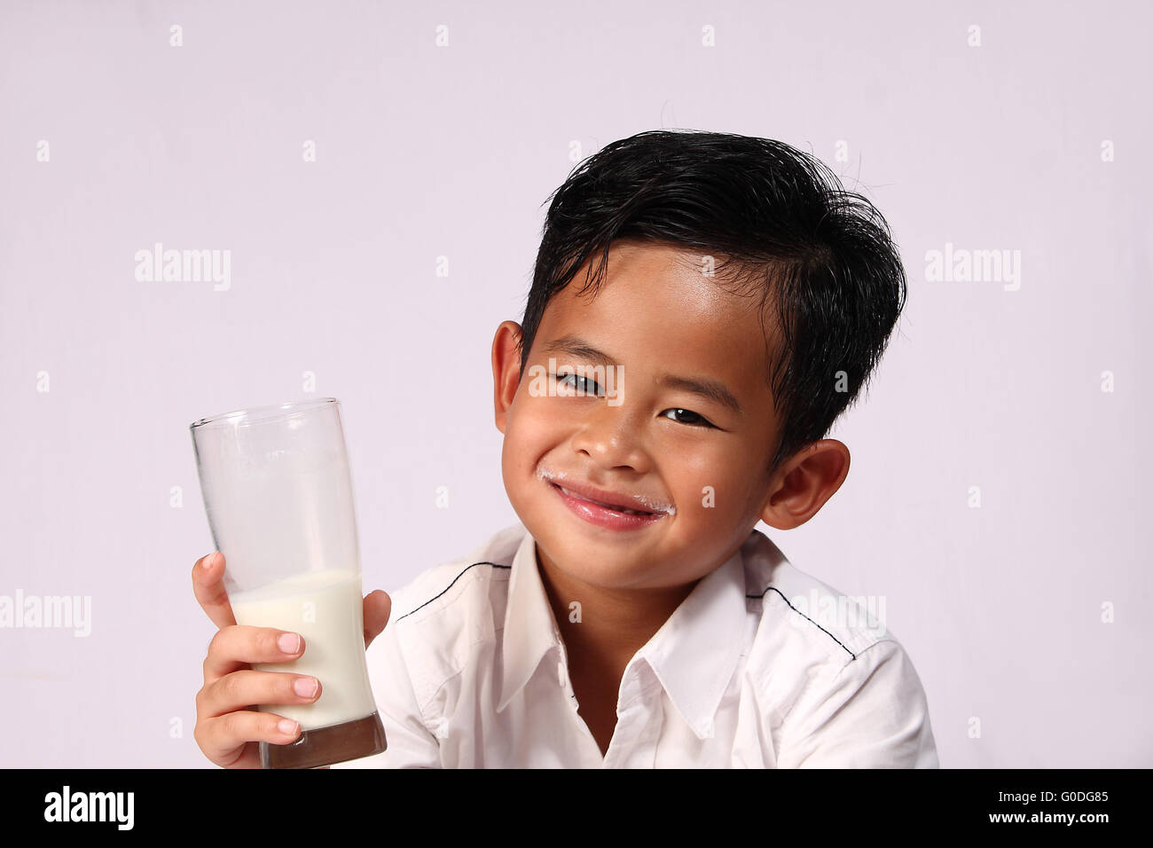 Felice e sorridente ragazzo asiatico che mostra un bicchiere di latte Foto Stock