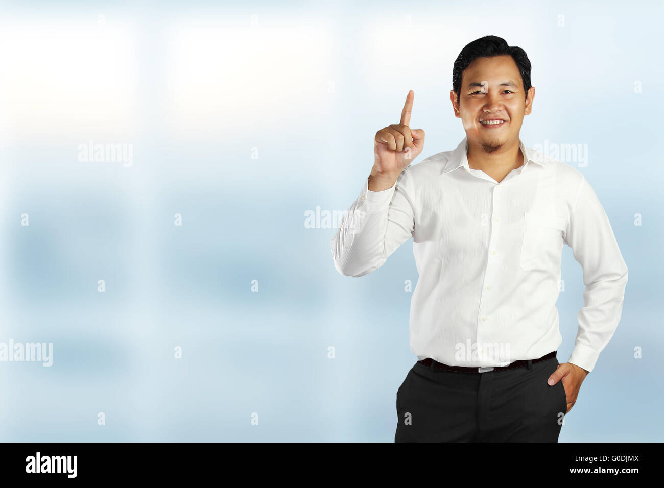 Giovane maschio asiatici in piedi e sorridente mostra il numero uno gesto con il suo dito puntato su sfondo lucido Foto Stock