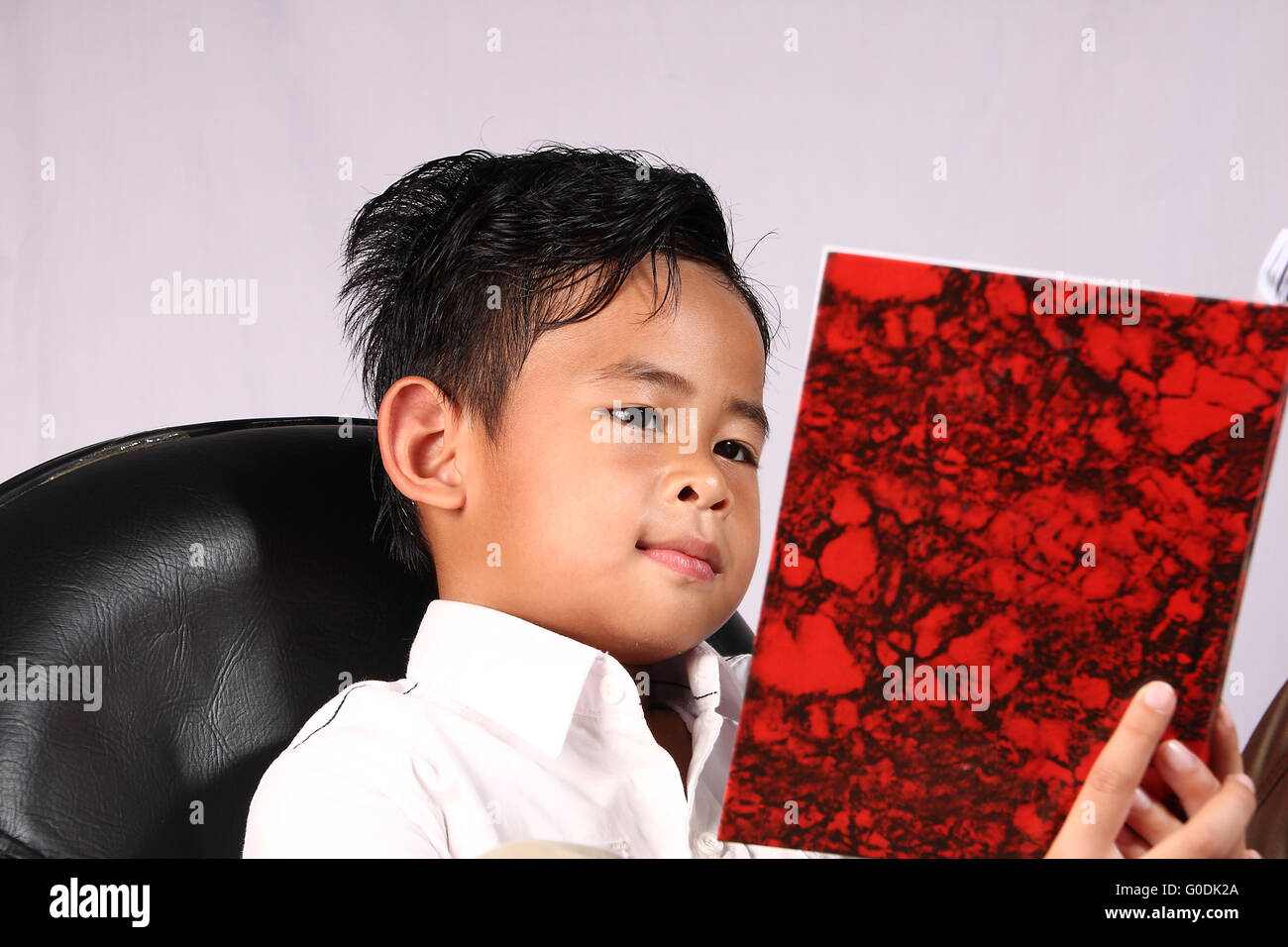 Smart Asian ragazzo lettura libro mentre è seduto su una sedia Foto Stock