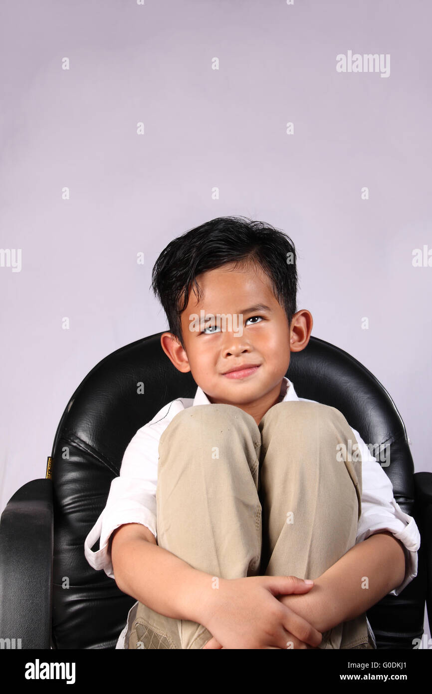 Felice ragazzo asiatico sorridente e sognare mentre è seduto su una sedia Foto Stock
