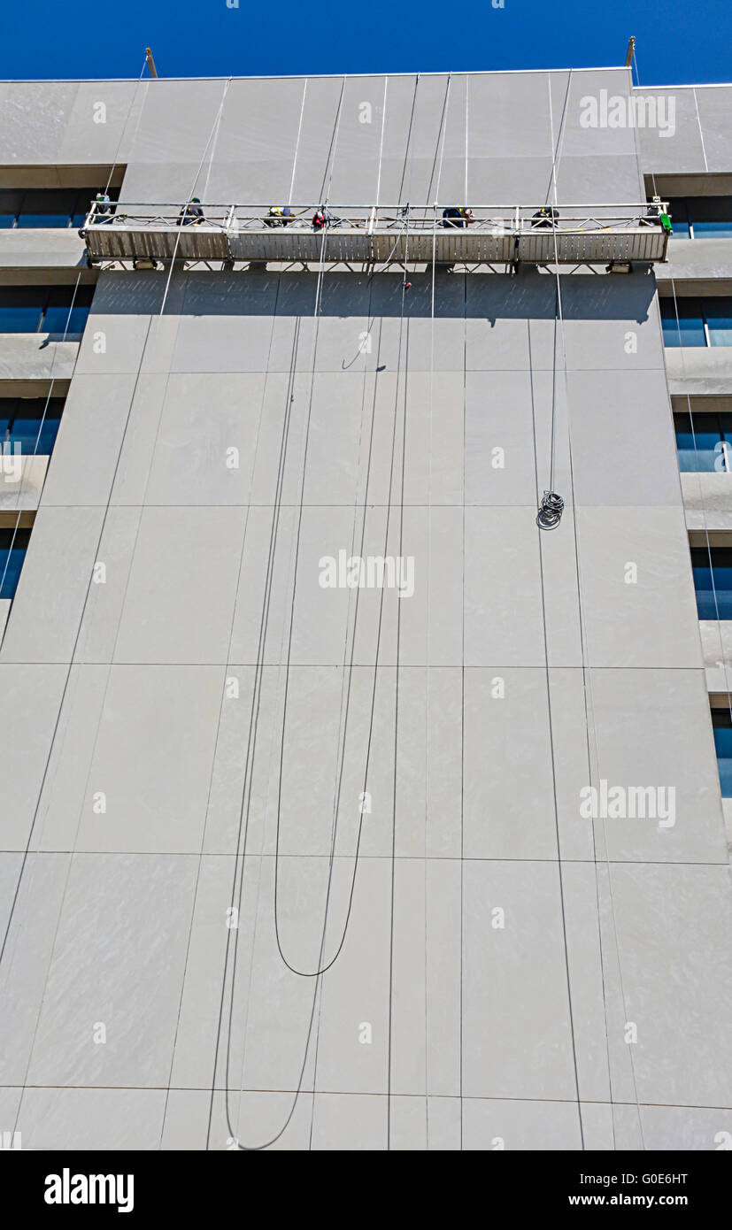 Un Ponteggio sospeso piattaforma alto sopra la strada a un alto edificio con gli uomini al lavoro per pulire l'edificio Foto Stock