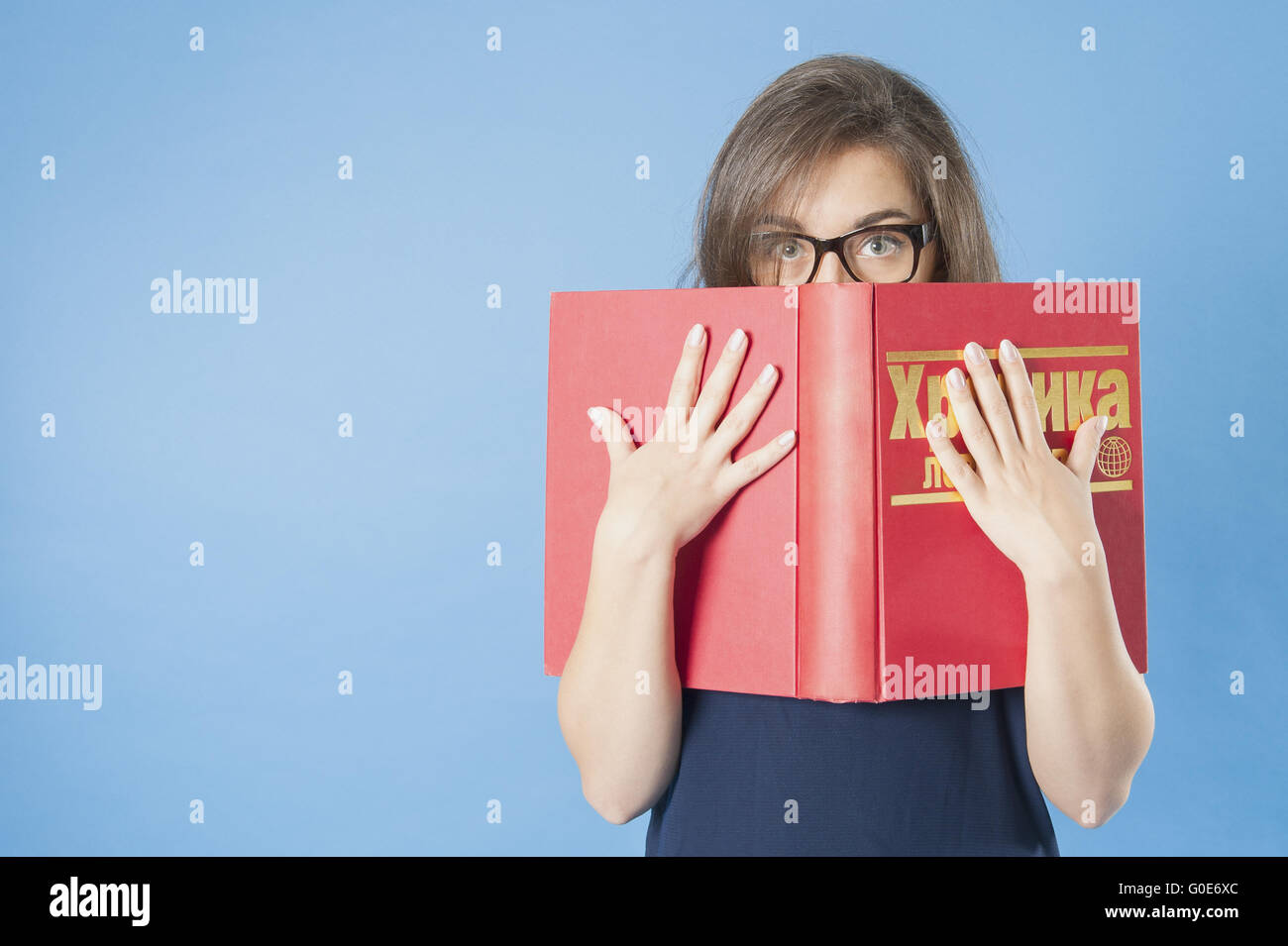 Ragazza con gli occhiali fa capolino da dietro un grande libro. Foto Stock
