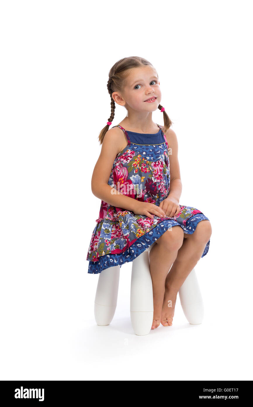 Piccola ragazza in un abito colorato su una sedia in studio e timidi Foto Stock