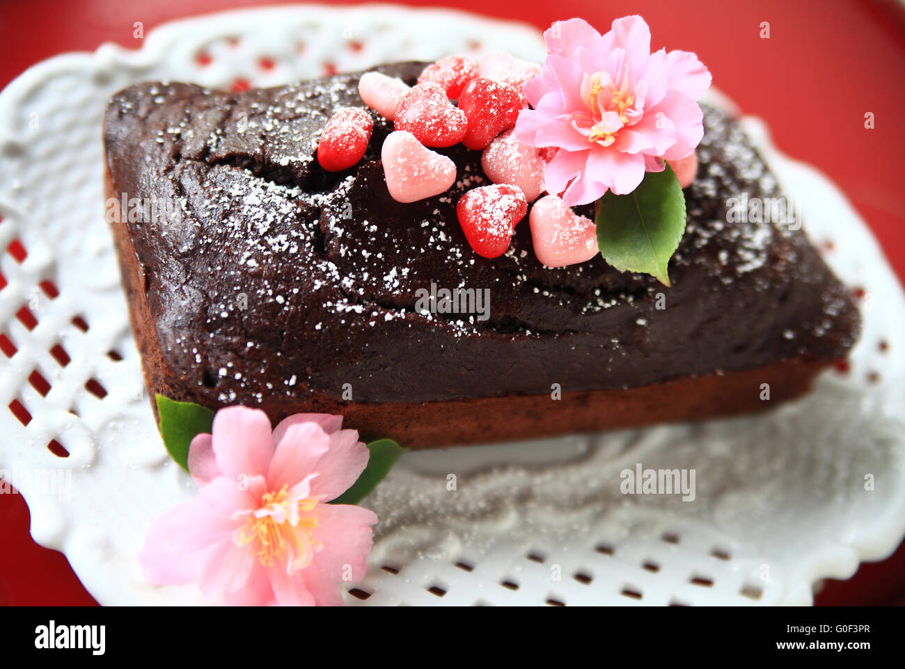 Torta al cioccolato con zucchero a velo, a forma di cuore di caramelle e fiori freschi Foto Stock
