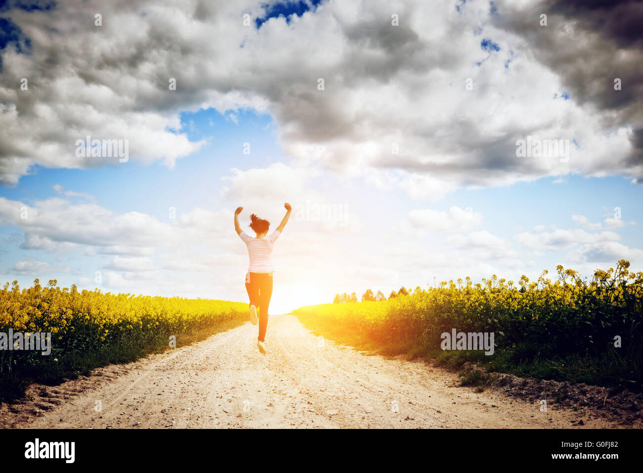 Felice giovane donna correre e saltare di gioia verso il sole sul campo primaverile dei concetti di successo Foto Stock