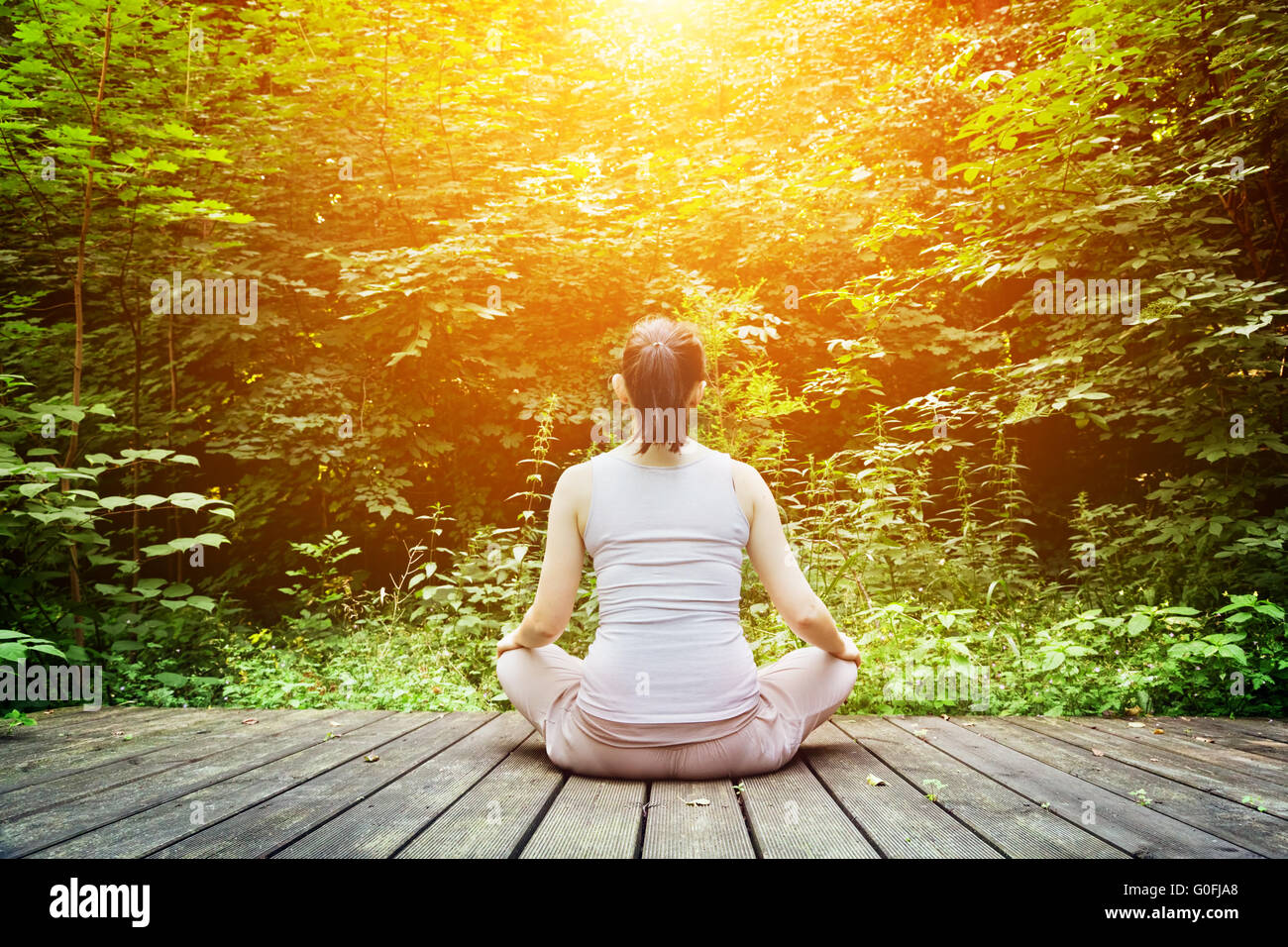 Giovane donna meditando in una foresta seduto su un pavimento di legno. Zen Foto Stock