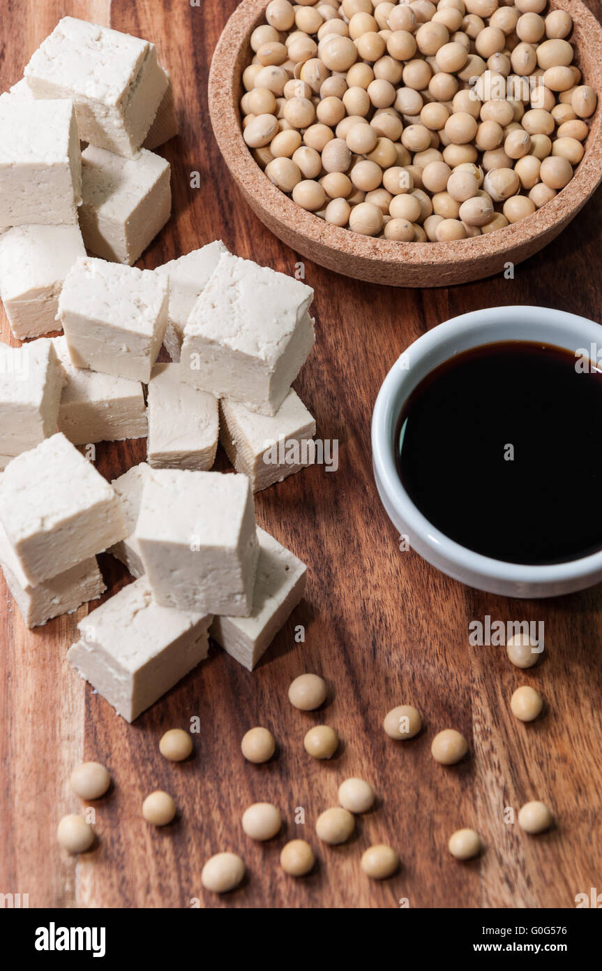 La salsa di soia, un pezzo di tofu e semi di soia su una tavola di legno Foto Stock