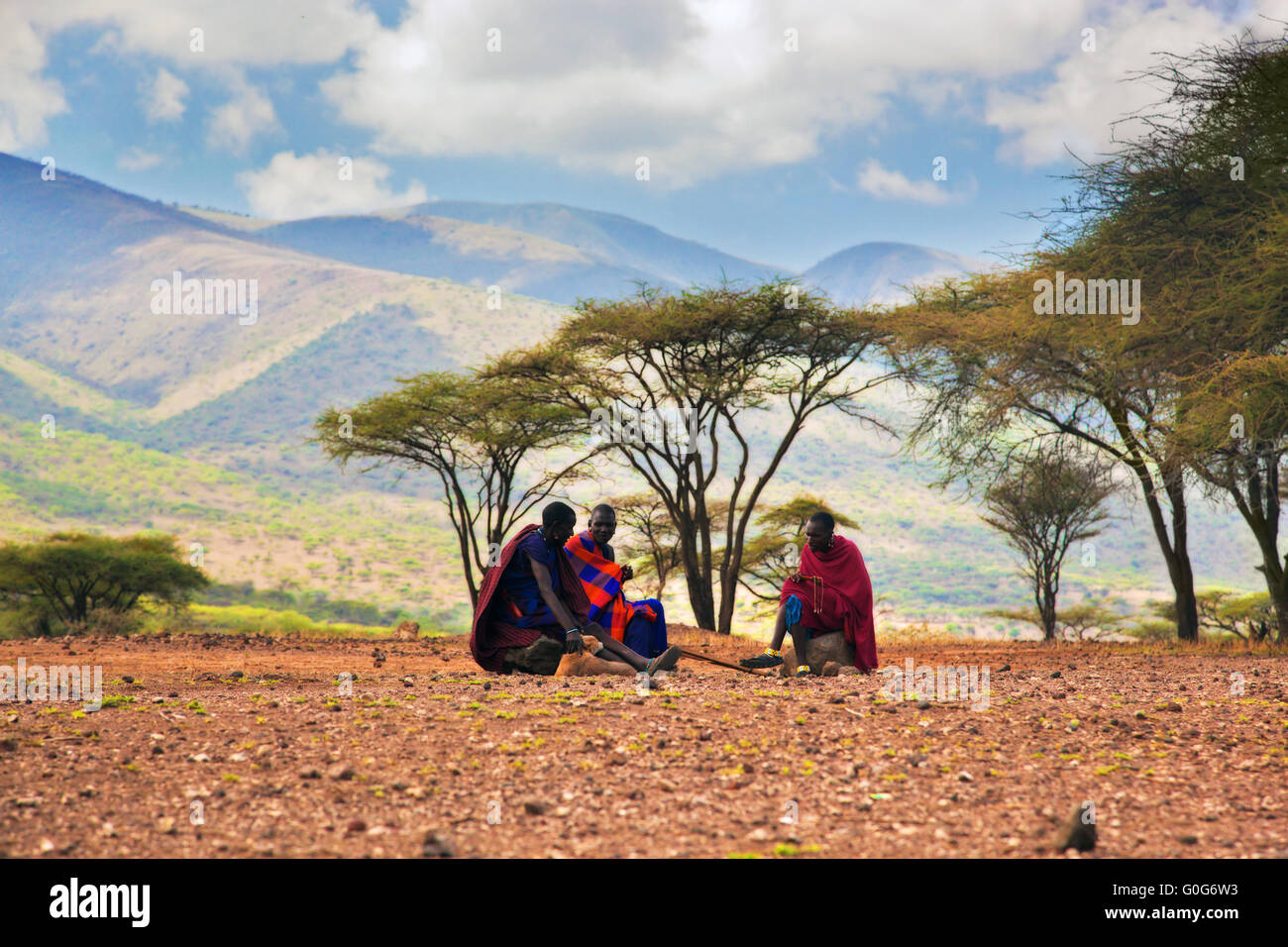 Maasai uomini seduti. Savana paesaggio in Tanzania, Africa Foto Stock