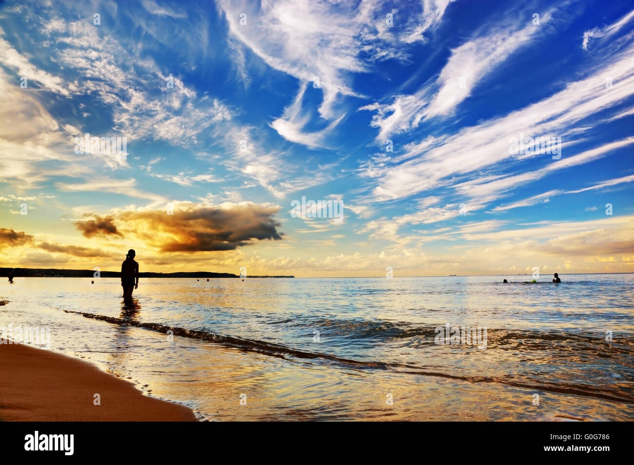 Donna in piedi nella calma oceano drammatica sotto il cielo al tramonto. Estate Foto Stock