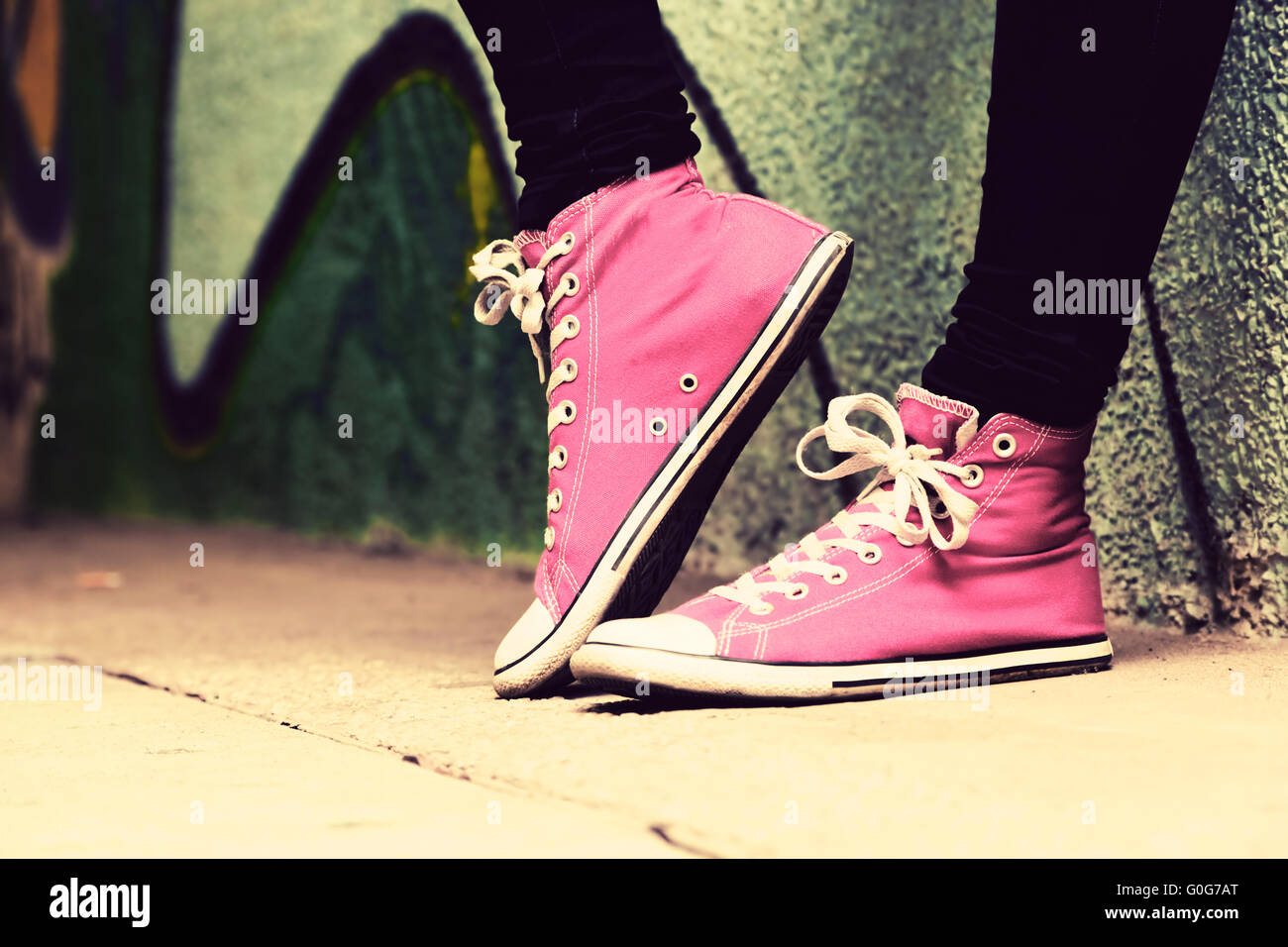 Close up di rosa sneakers indossata da un adolescente. Grunge muro di graffiti Foto Stock