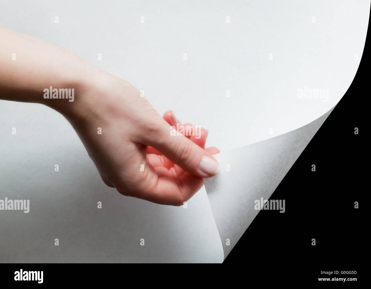 La mano tirando un basso angolo di carta per scoprire Foto Stock