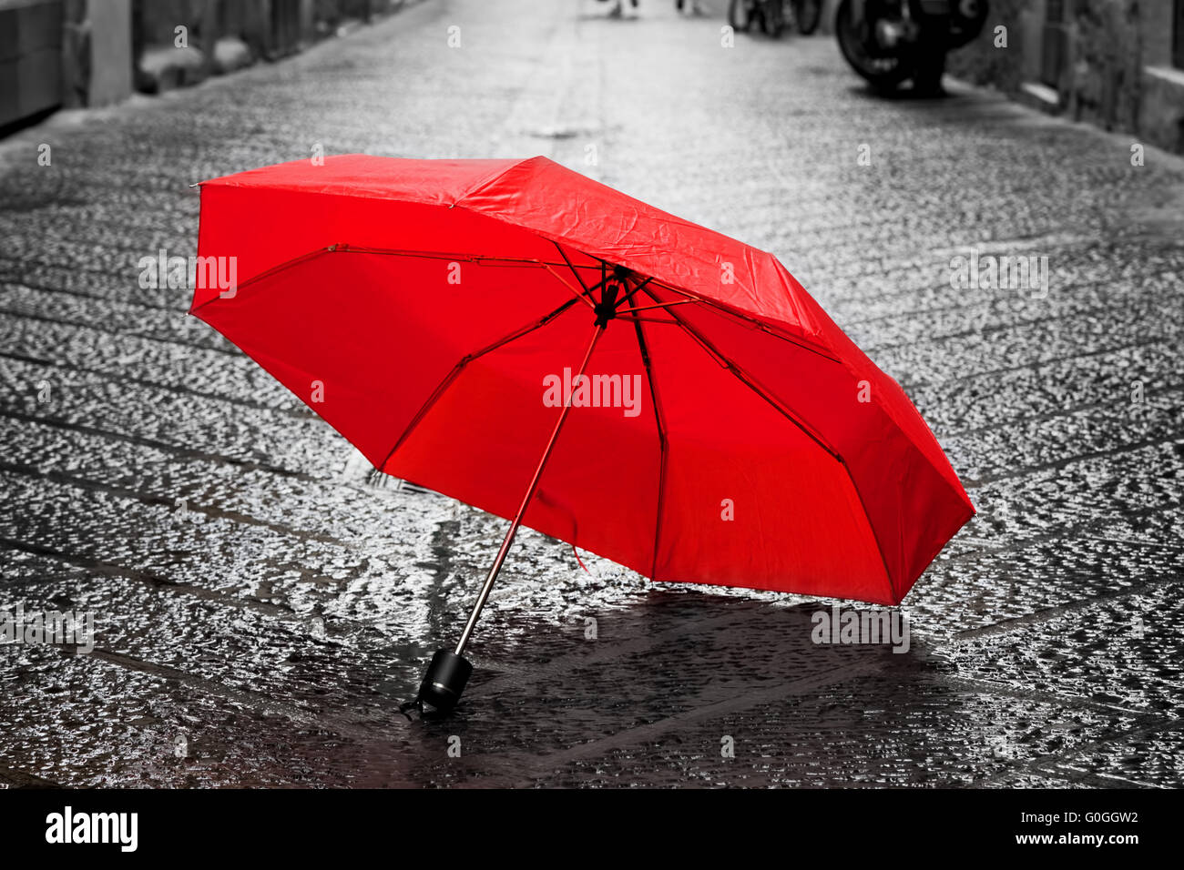 Ombrellone rosso su strada di ciottoli della città vecchia. Vento e pioggia Foto Stock