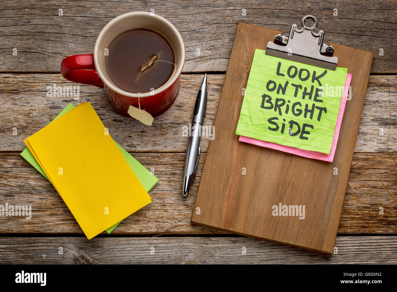 Guardare il lato luminoso di consulenza o di promemoria - nota adesiva su una clipboard con una tazza di tè Foto Stock