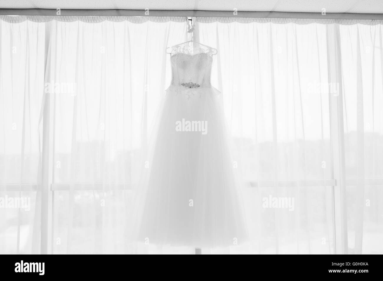 Bella bianco abito da sposa appeso da una finestra Foto Stock