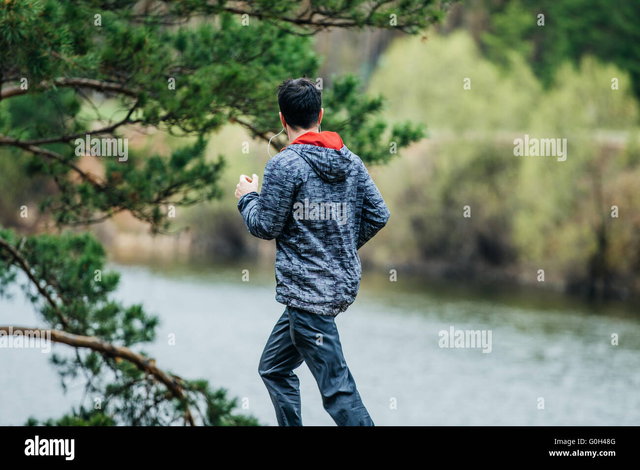 Atleta giovane uomo che corre su strada nella primavera del parco. Ascolto di musica sulle cuffie Foto Stock