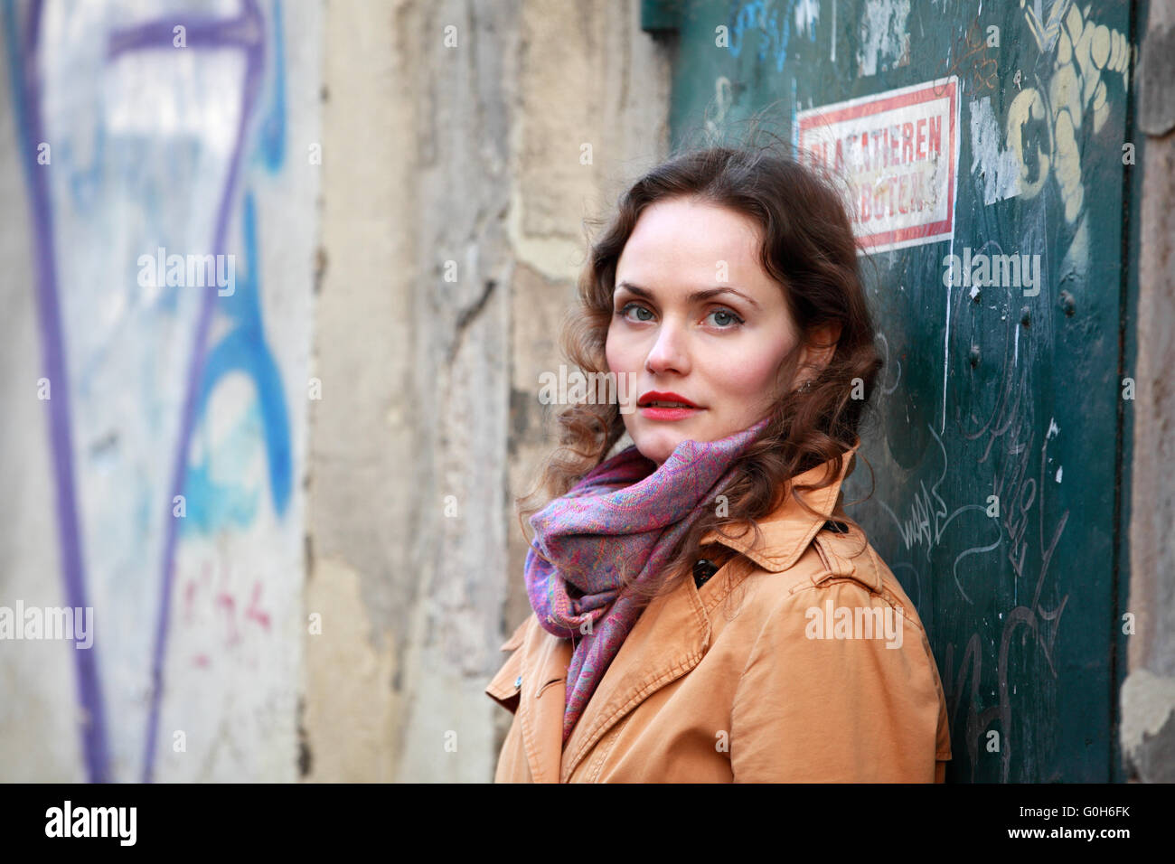 Bella bruna donna con rivestimento beige classifica in una casa con graffiti Foto Stock