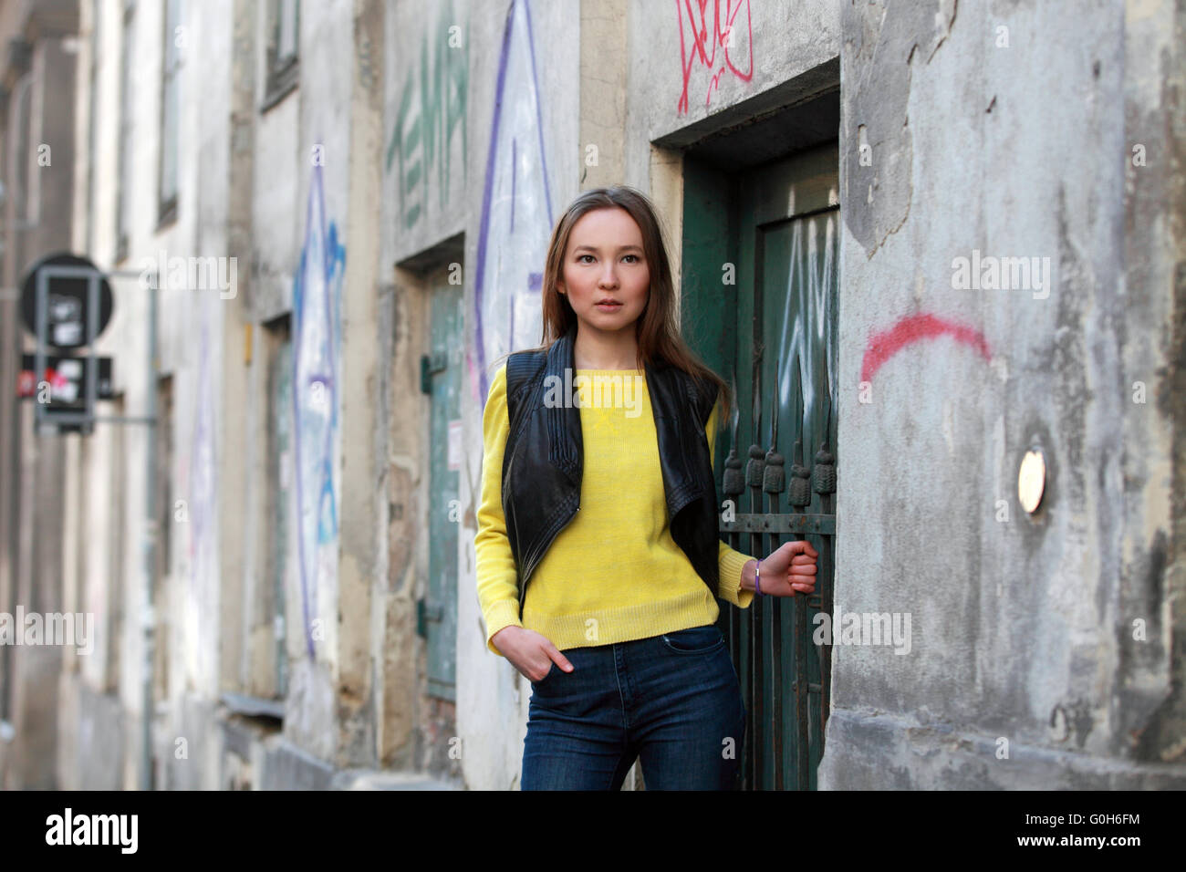 Bella donna asiatica in maglione giallo e jeans in piedi in una casa con graffiti Foto Stock