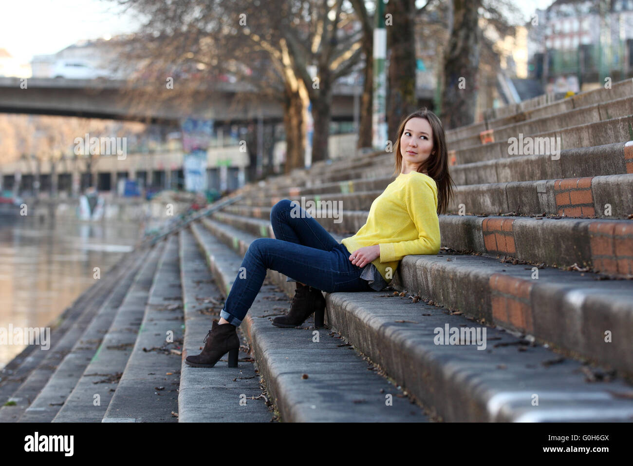 Bella donna asiatica in felpa gialla seduti su un fiume in una città europea Foto Stock