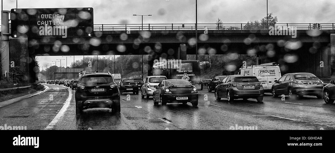 Accodamento di traffico su autostrada con matrice di overhead segno indicante coda attenzione leggermente sfocato dalle gocce di pioggia sul parabrezza Foto Stock