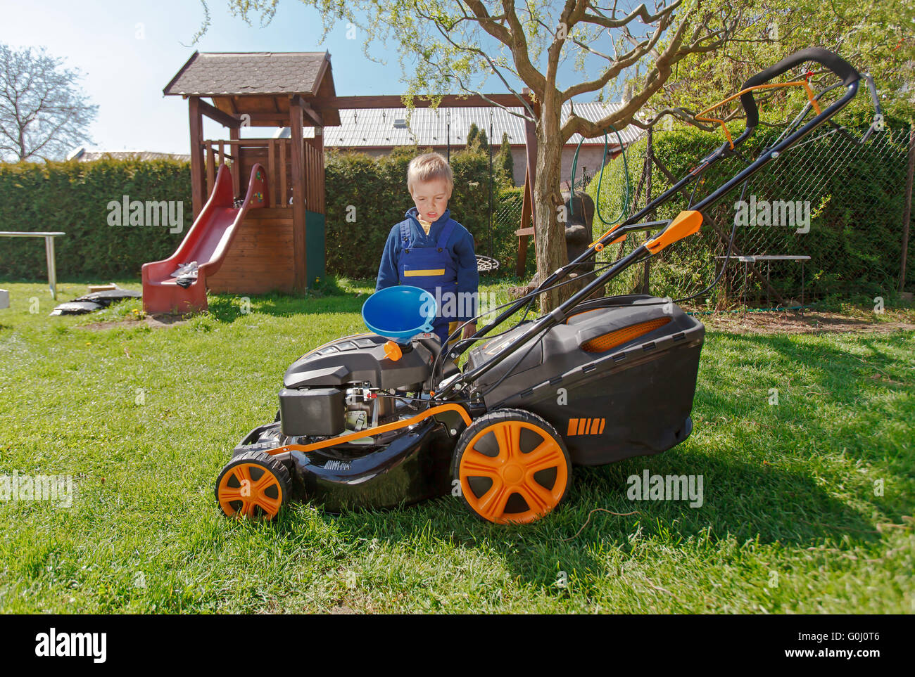 Carino, Little Boy mows prato. boy ispeziona la falciatrice, prima di guidare o di sinistra dell'olio motore. Foto Stock