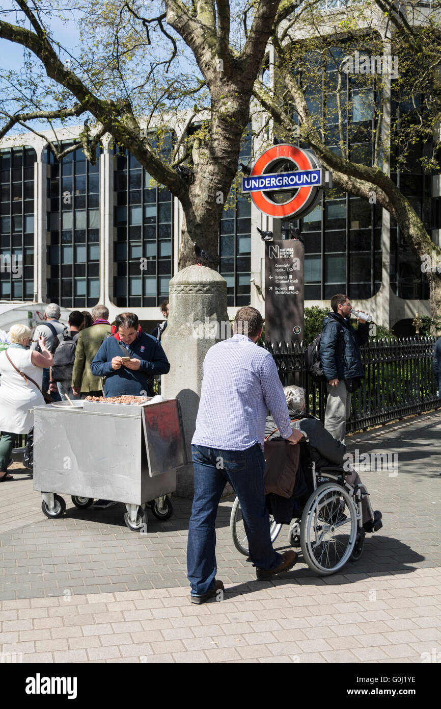 Una persona con disabilità e il suo accompagnatore fuori dal National History Museum nel quartiere dei musei di Londra a South Kensington, Londra, Inghilterra, Regno Unito Foto Stock