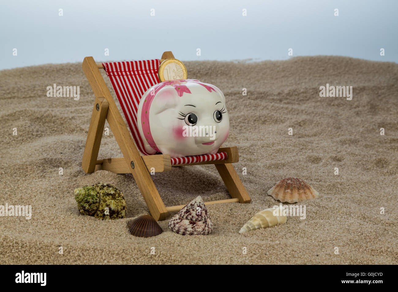 Sdraio sulla spiaggia con il salvadanaio e euro Foto Stock