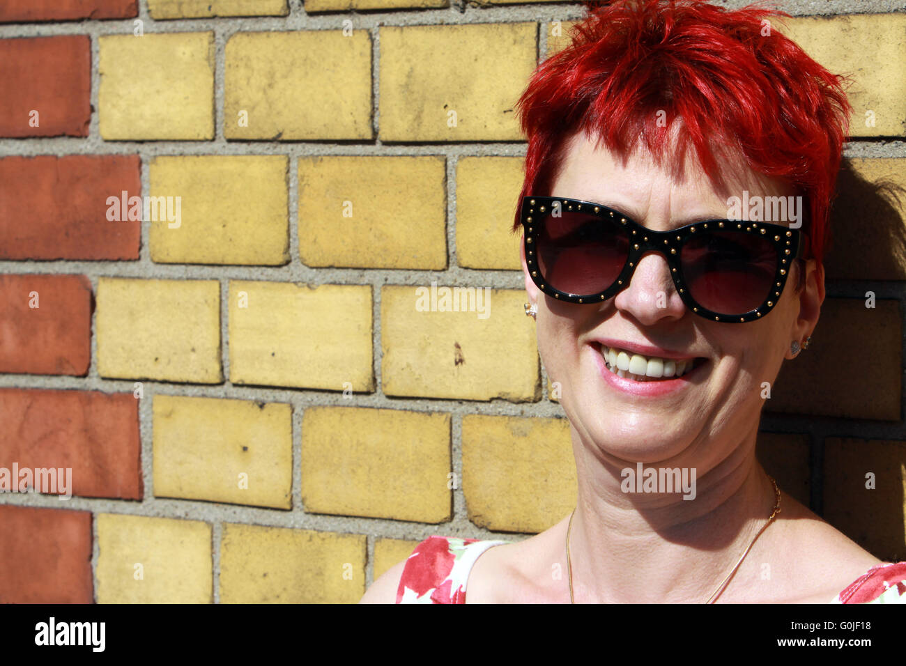 I capelli rossi donna appoggiata contro un muro di mattoni Foto Stock